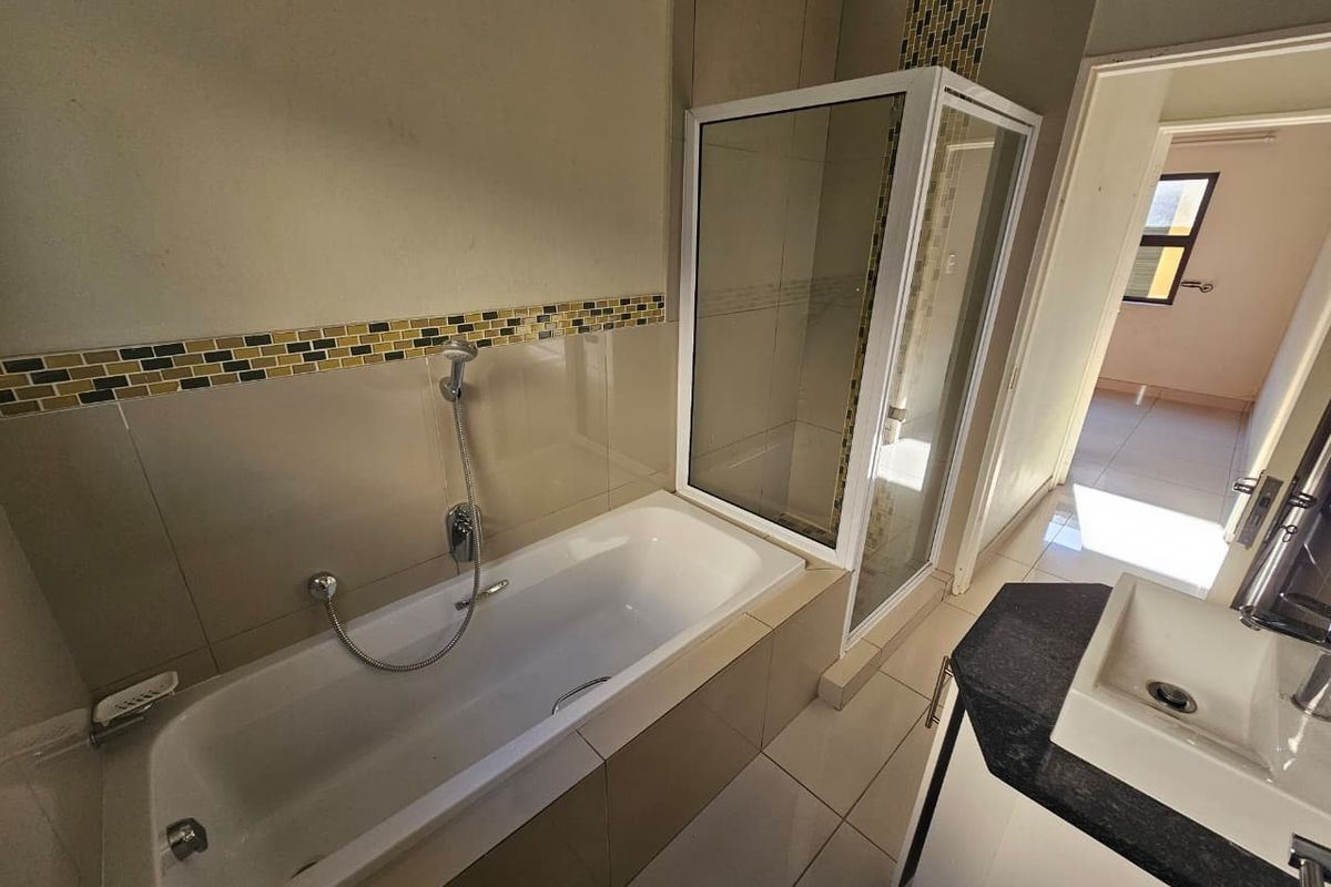 A functional bathroom featuring a built-in bathtub, a separate glass-enclosed shower, and a vanity basin with a dark countertop.