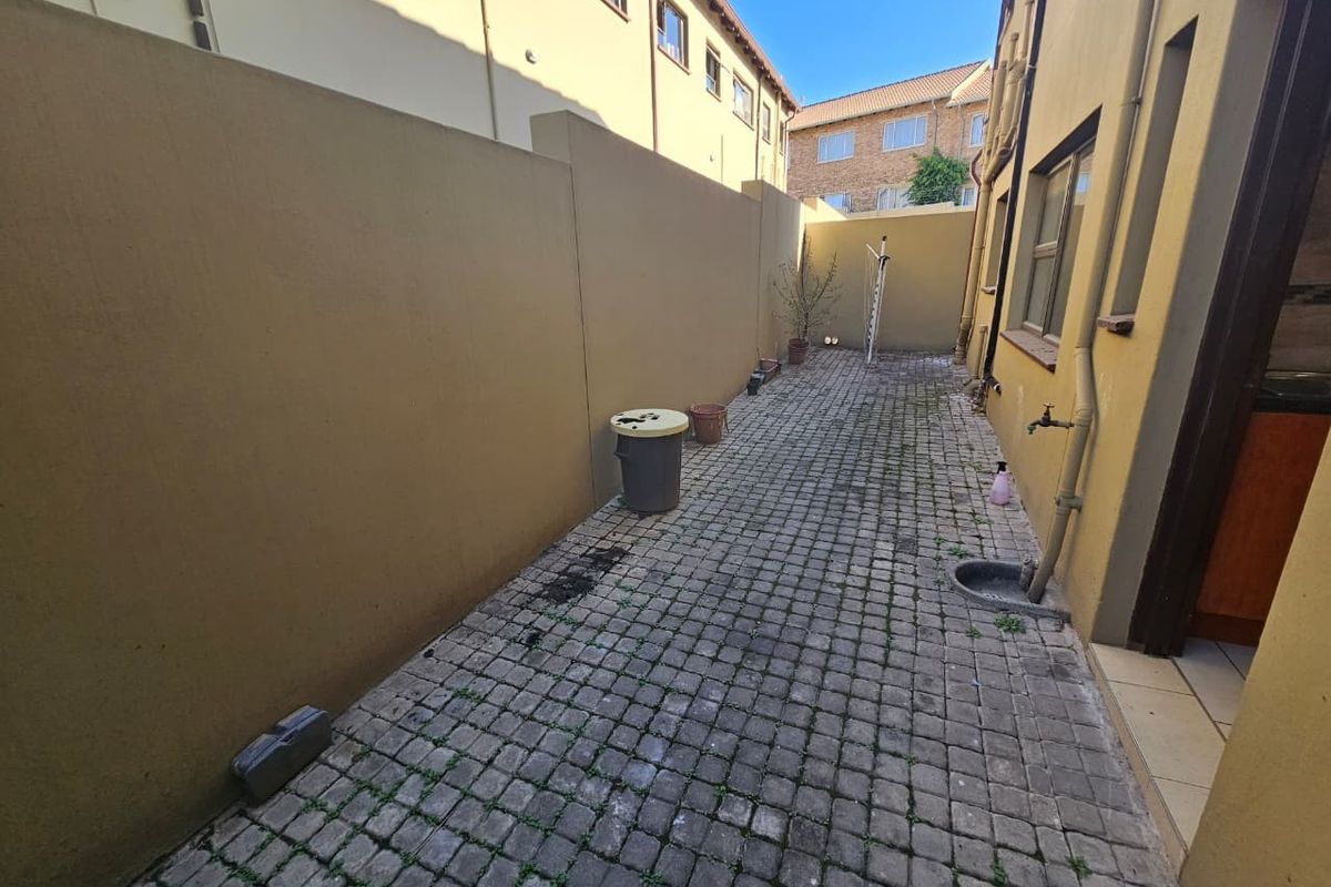 A narrow side courtyard featuring paved flooring, an exterior water tap, and high boundary walls, providing a functional utility space for the townhouse.
