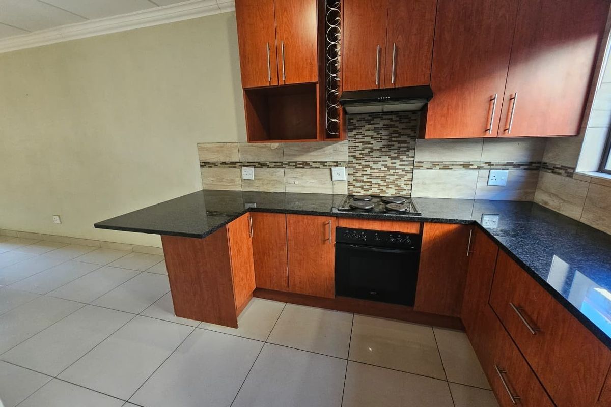 A functional kitchen featuring wood-finish cabinetry, dark granite countertops, a built-in oven, electric hob, extractor fan, and tiled flooring.