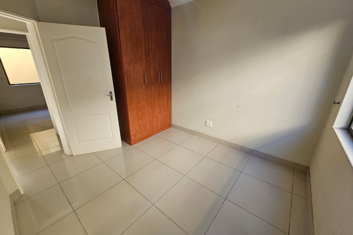 A bright, empty bedroom featuring neutral floor tiles, a built-in wooden wardrobe, and a standard interior door leading to a hallway.
