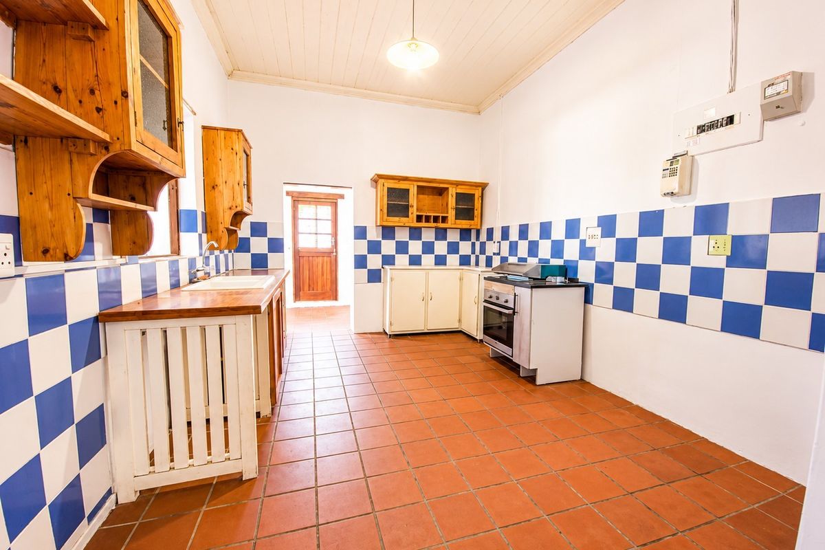 A functional kitchen featuring terracotta flooring, timber cabinetry, a tiled splashback, and a freestanding stove, offering potential for modern updates.