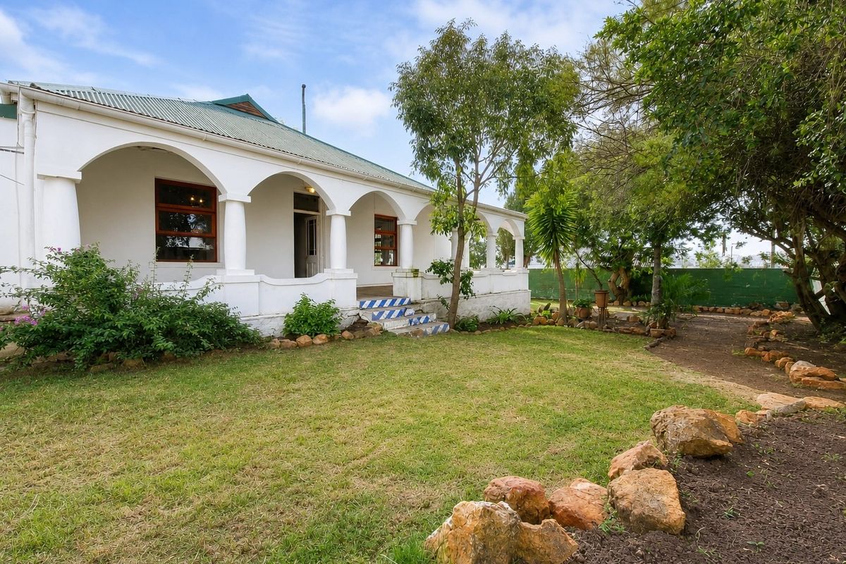 A charming rear elevation featuring a spacious covered veranda with classic arched columns, overlooking a well-maintained garden with stone landscaping.