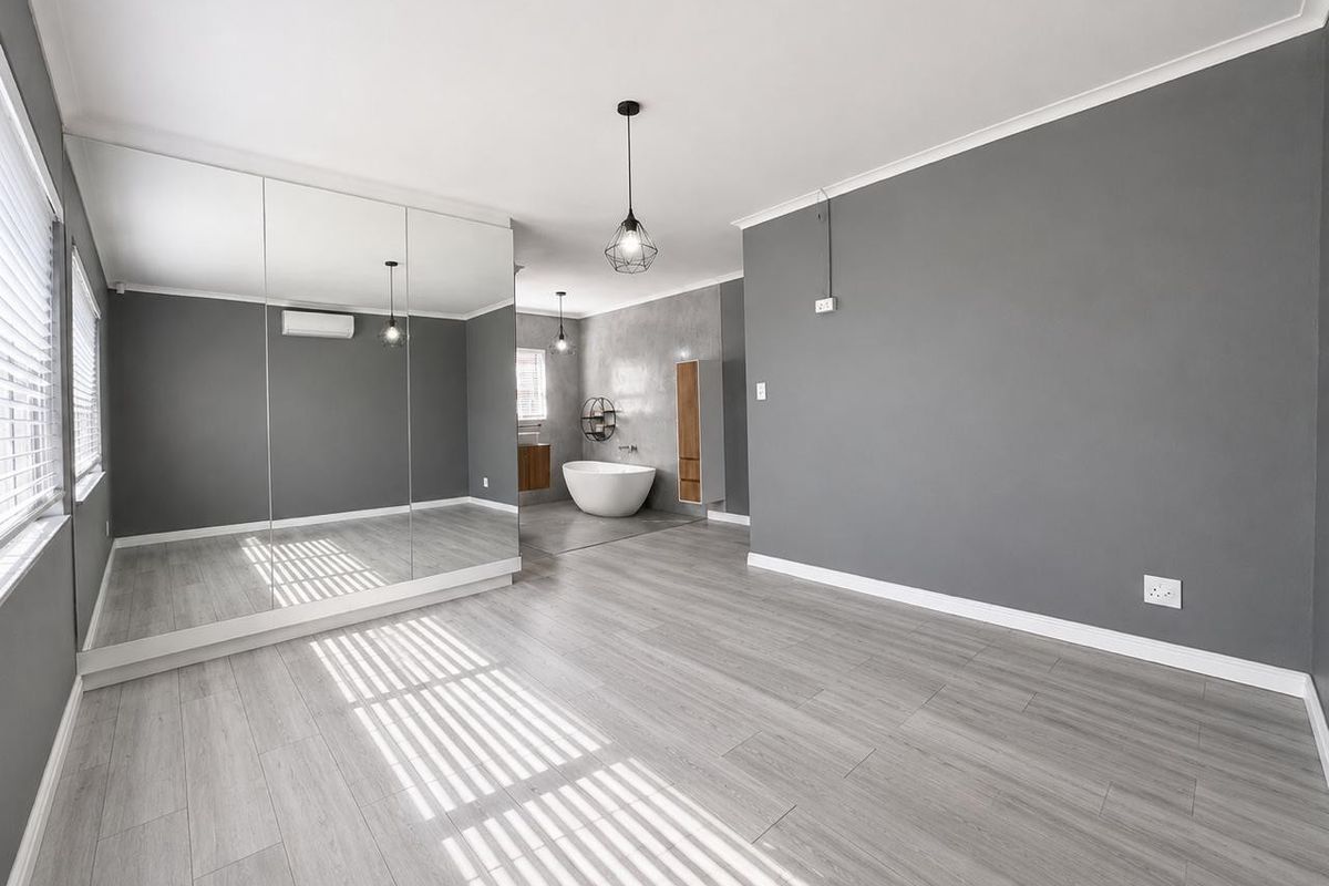 Spacious bedroom featuring light wood-look flooring, mirrored built-in wardrobes, and an open-plan ensuite area with a modern freestanding bathtub.