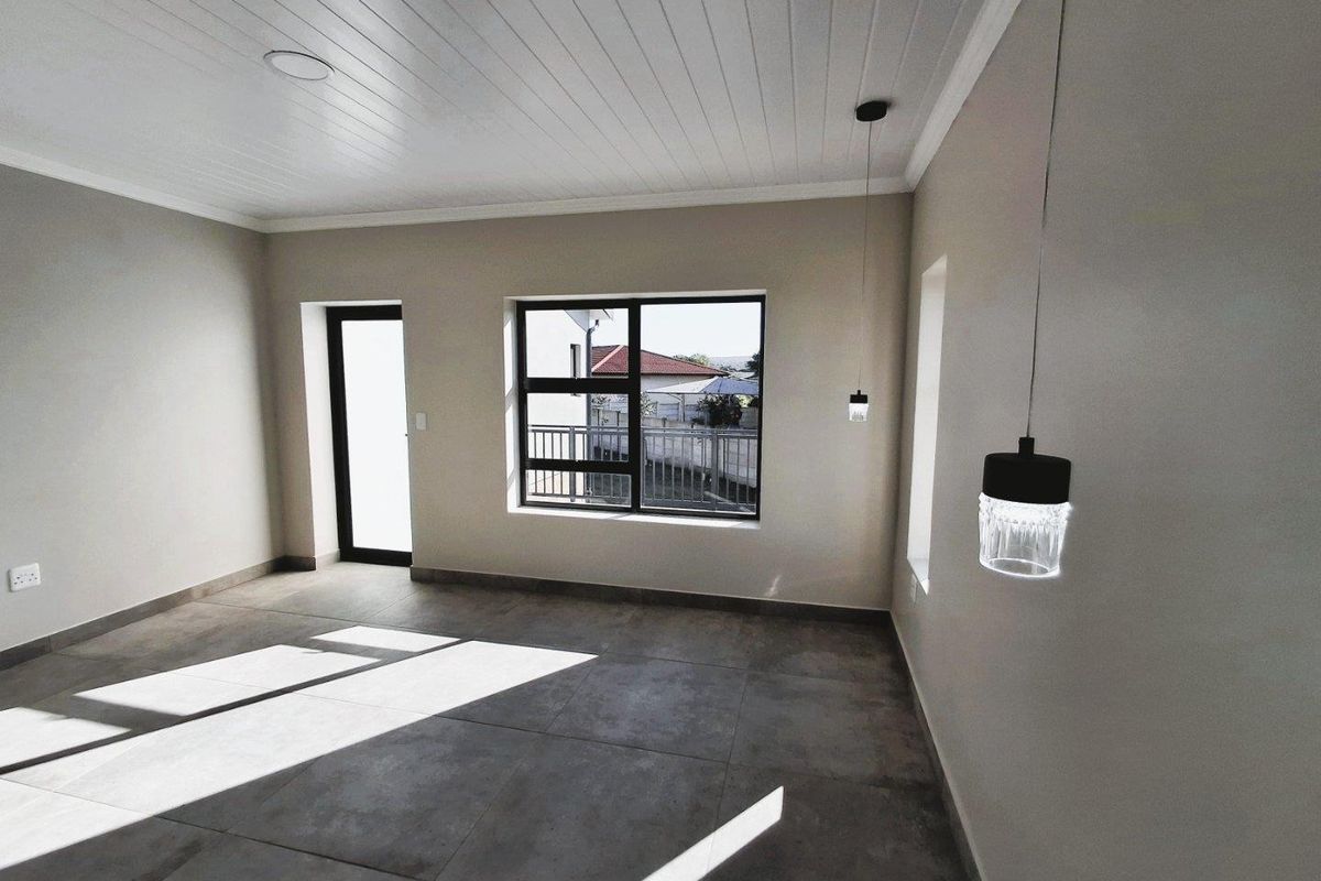 A bright, modern living area featuring large windows, tiled flooring, and contemporary pendant lighting, offering a clean and neutral space ready for personalization.