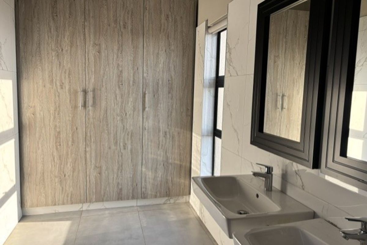 Modern bathroom featuring dual wall-mounted sinks, large framed mirrors, and extensive built-in wood-finish cabinetry providing ample storage space.