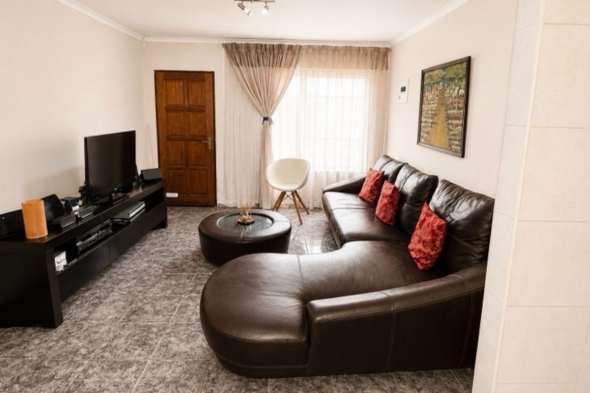 A comfortable living room featuring tiled flooring, a wooden door, and large windows that allow for natural light.