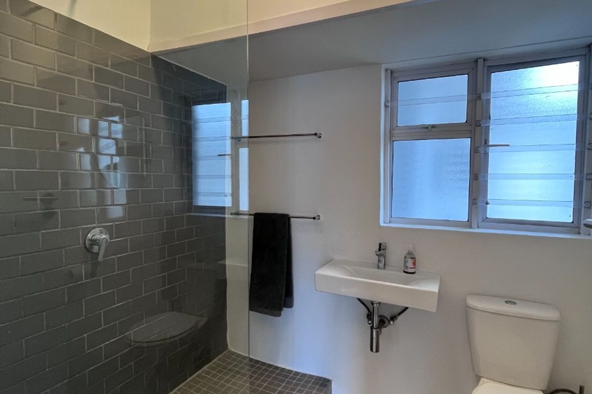 Modern bathroom featuring a walk-in shower with grey subway tiles, a wall-mounted basin, and a toilet, complemented by louvered windows for natural ventilation.