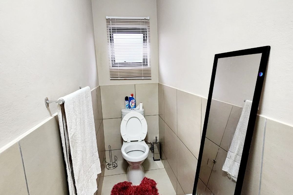 A compact guest bathroom featuring neutral wall and floor tiling, a standard toilet, and a small window with a venetian blind.