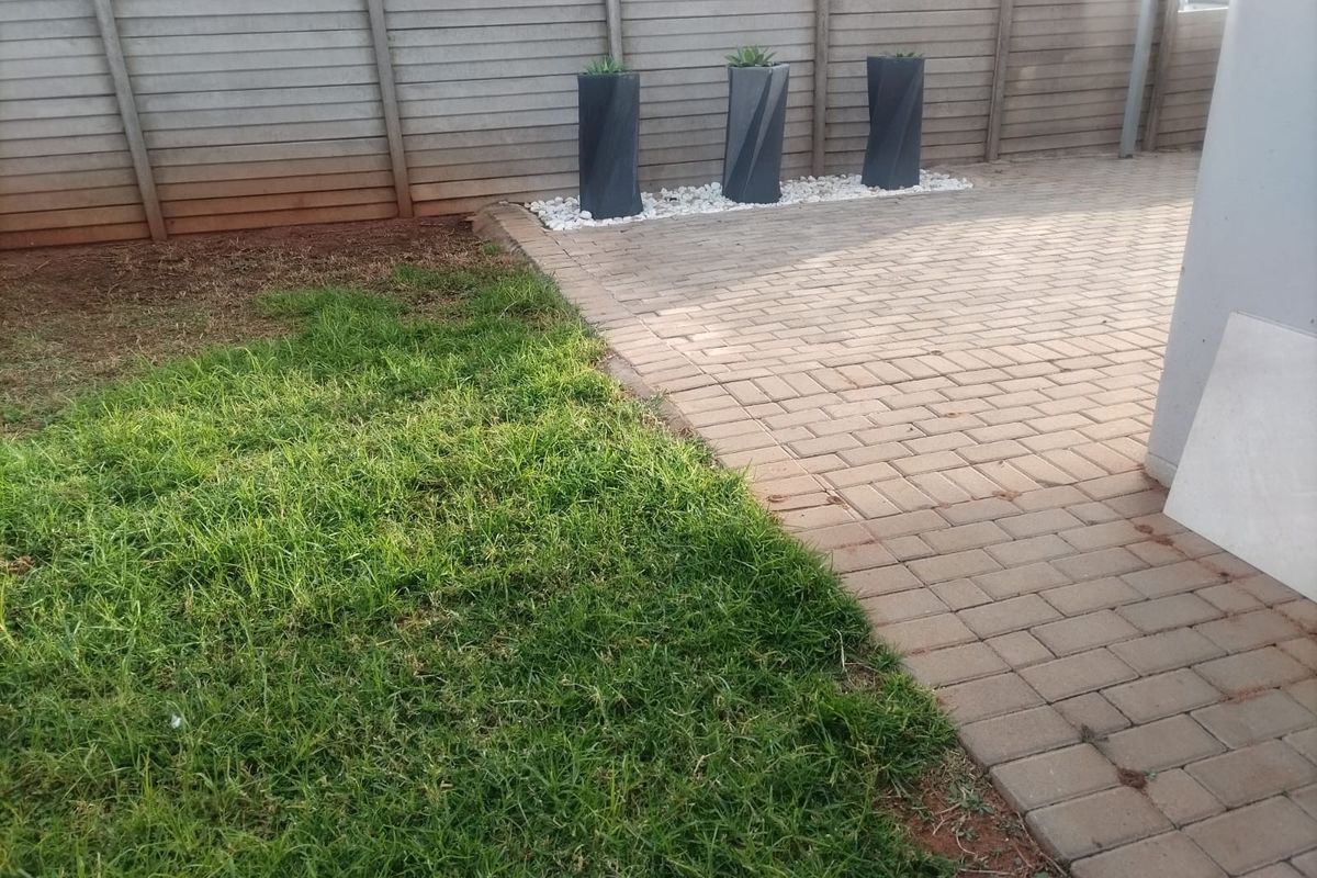 A rear garden area featuring a paved patio section, a small lawn, and a precast concrete boundary wall.