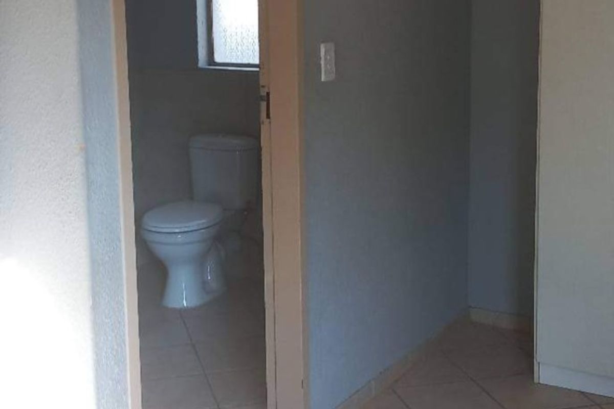 A view from a tiled hallway looking into a bathroom featuring a toilet and window.
