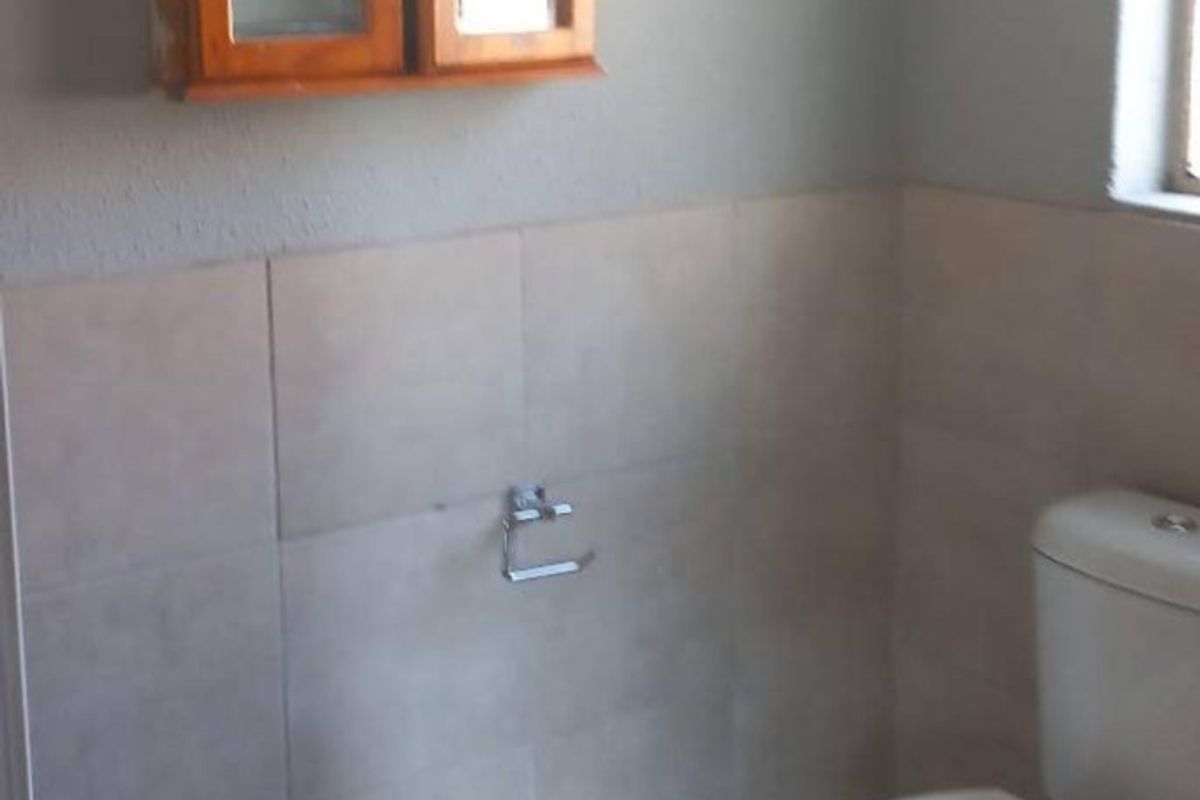 A functional bathroom featuring a standard toilet, wall-mounted cabinet, and neutral wall tiling.