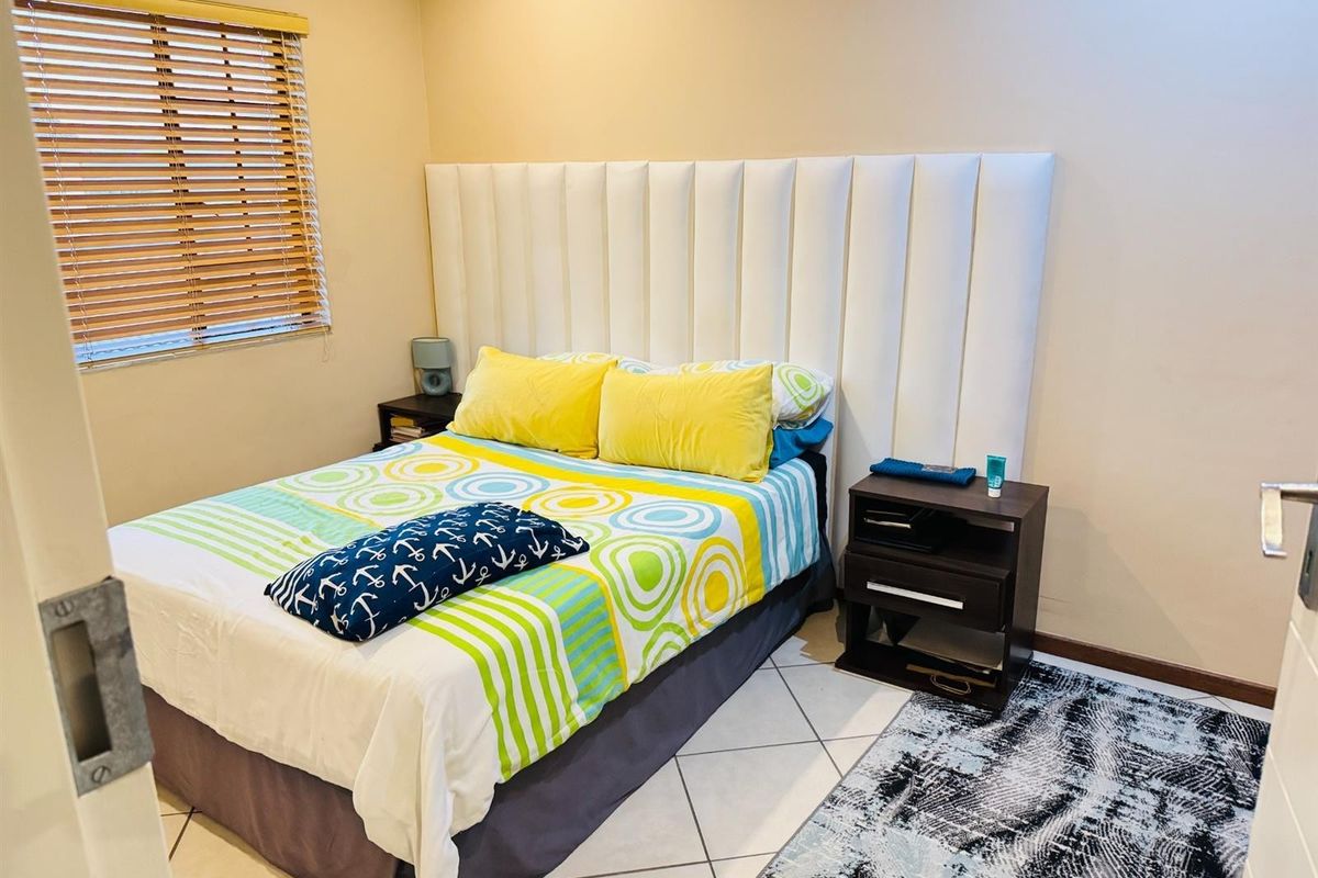 A functional bedroom featuring tiled flooring, a large vertical-panel headboard, and wooden venetian blinds.