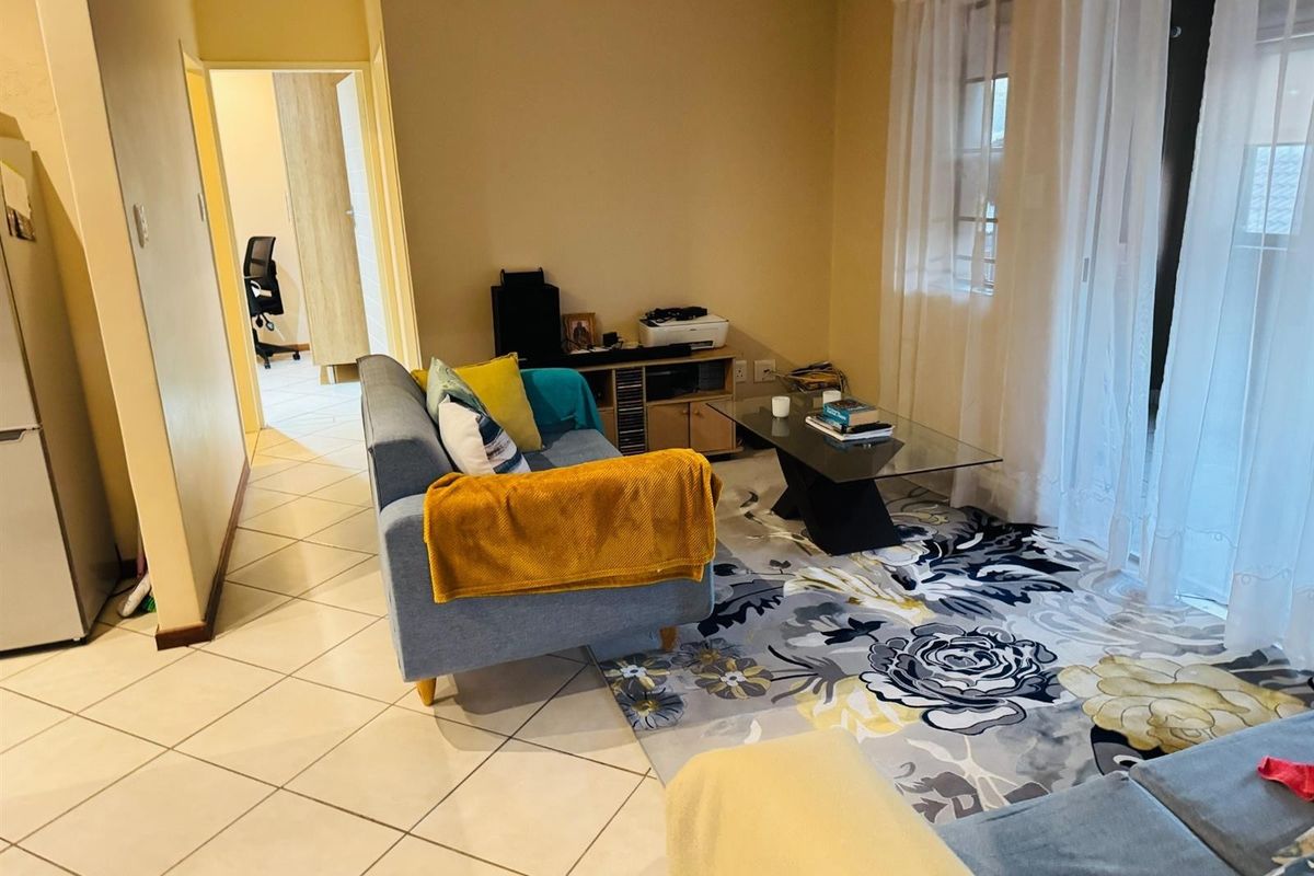 A living room area featuring tiled flooring and sliding glass doors leading to an outdoor space, with an adjacent hallway view.