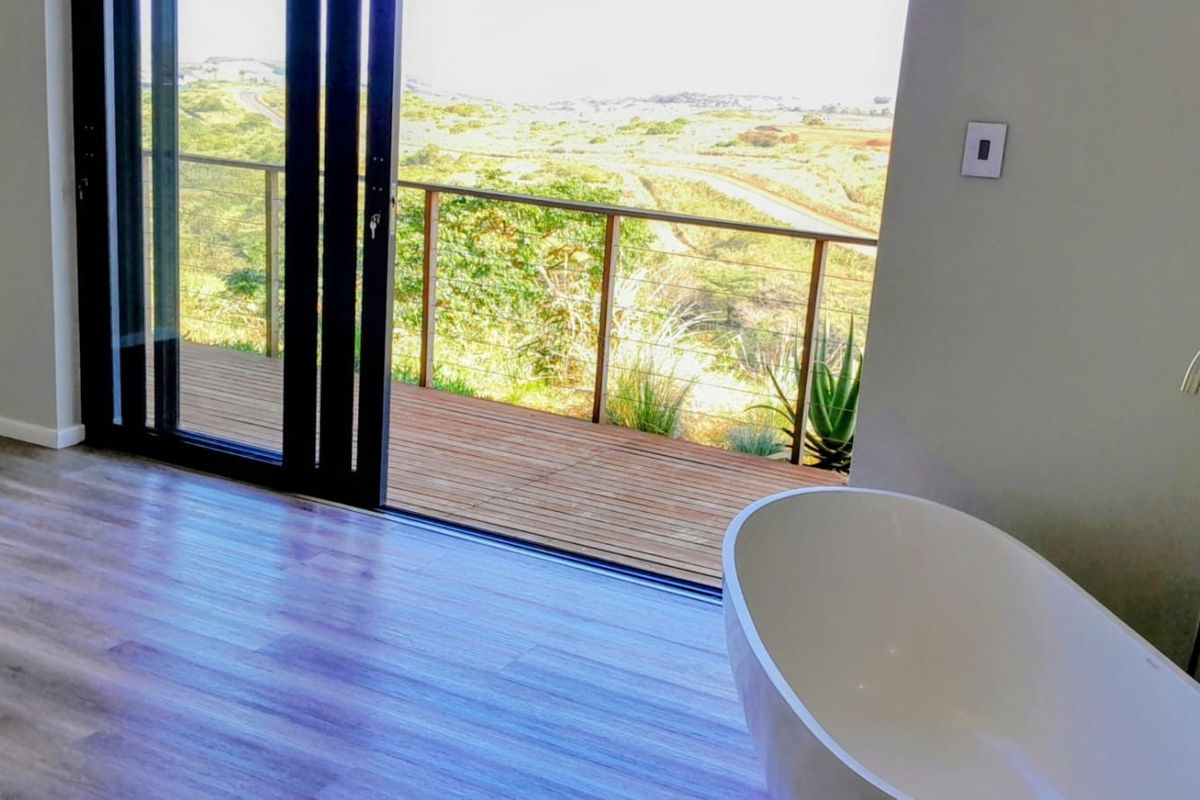 Modern bathroom featuring a freestanding bathtub and large sliding glass doors opening onto a wooden deck with scenic landscape views.