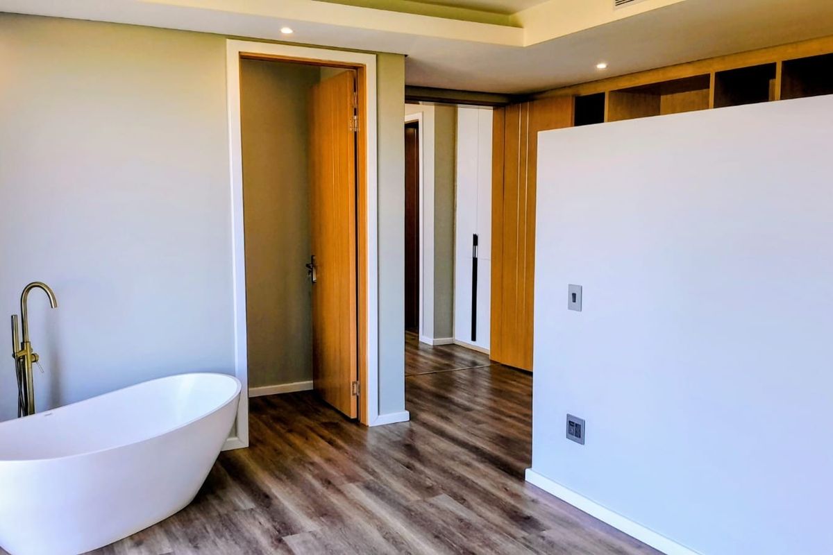 Modern primary bedroom suite featuring a freestanding bathtub with brass fixtures, wood-look flooring, and integrated built-in cabinetry.
