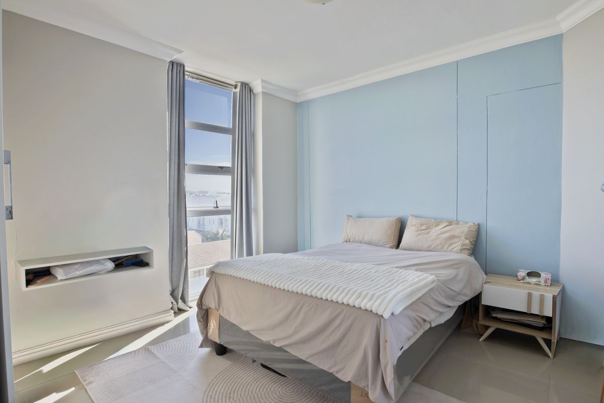 A bright bedroom featuring a built-in wall niche, large window with natural light, and neutral tiled flooring.