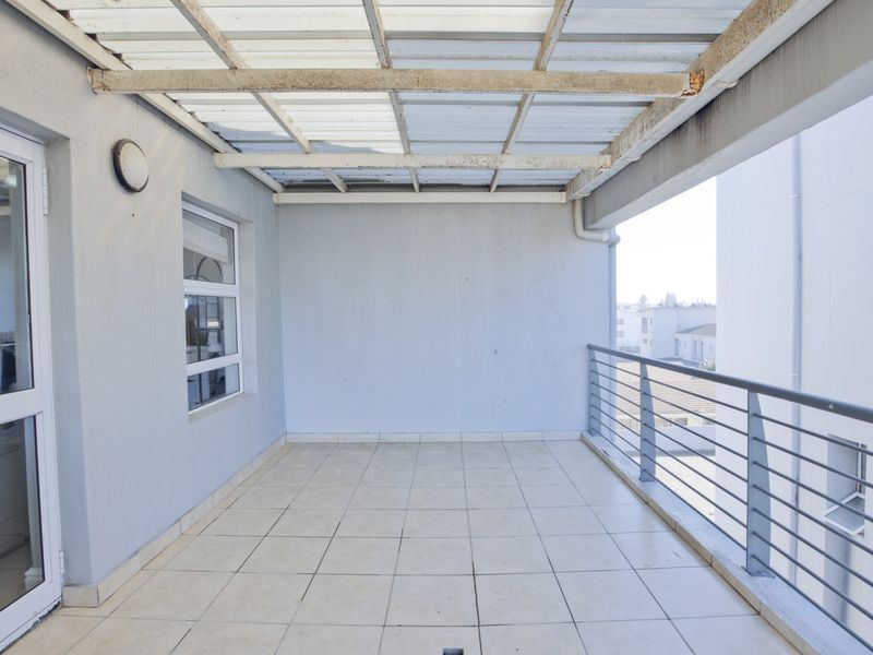 A spacious covered balcony featuring tiled flooring, a metal safety balustrade, and direct access to the interior via a sliding glass door.