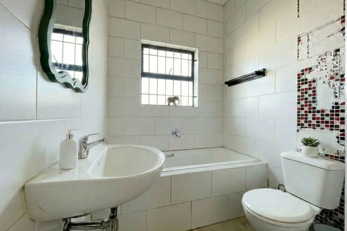 A compact bathroom featuring a white bathtub, wall-mounted basin, and toilet with white subway-style wall tiling and a decorative mosaic accent.