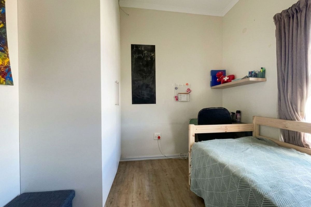 A functional bedroom featuring built-in cupboards, wood-look flooring, and a window with curtaining.