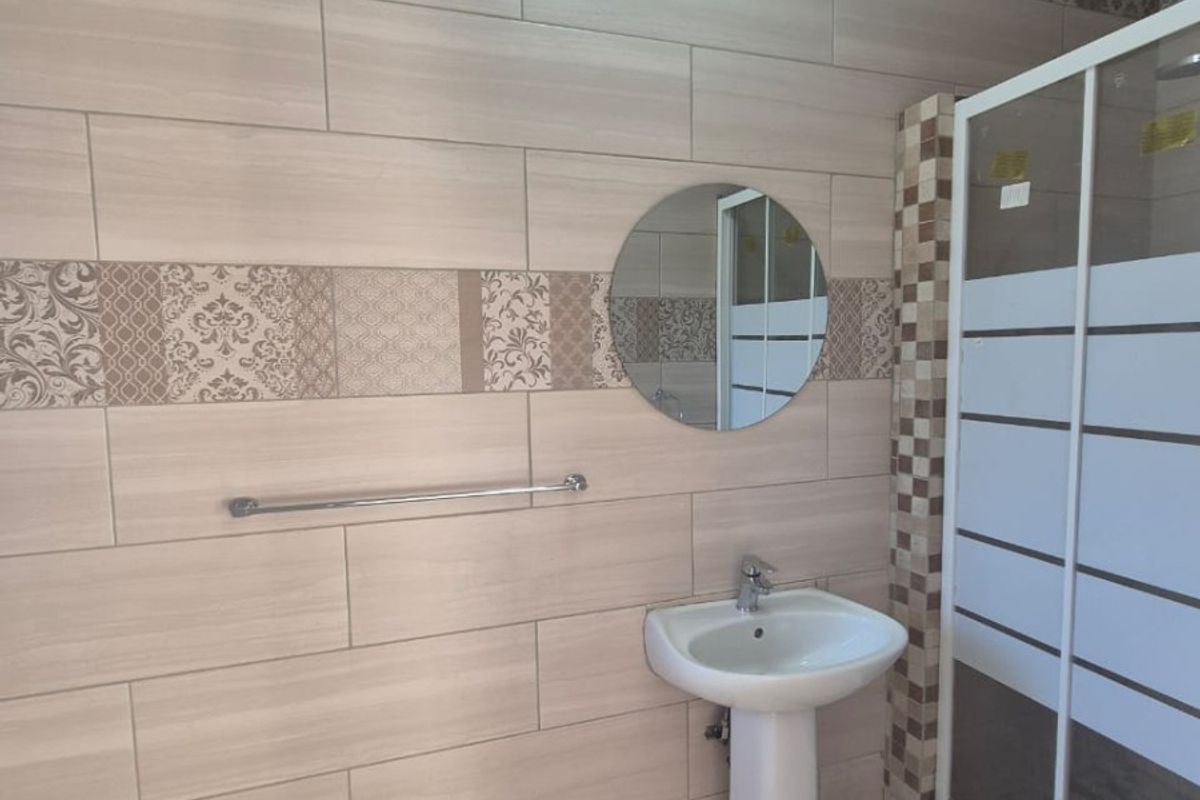 A well-maintained bathroom featuring a pedestal basin, a circular wall mirror, and a glass-enclosed shower with decorative tiled wall accents.