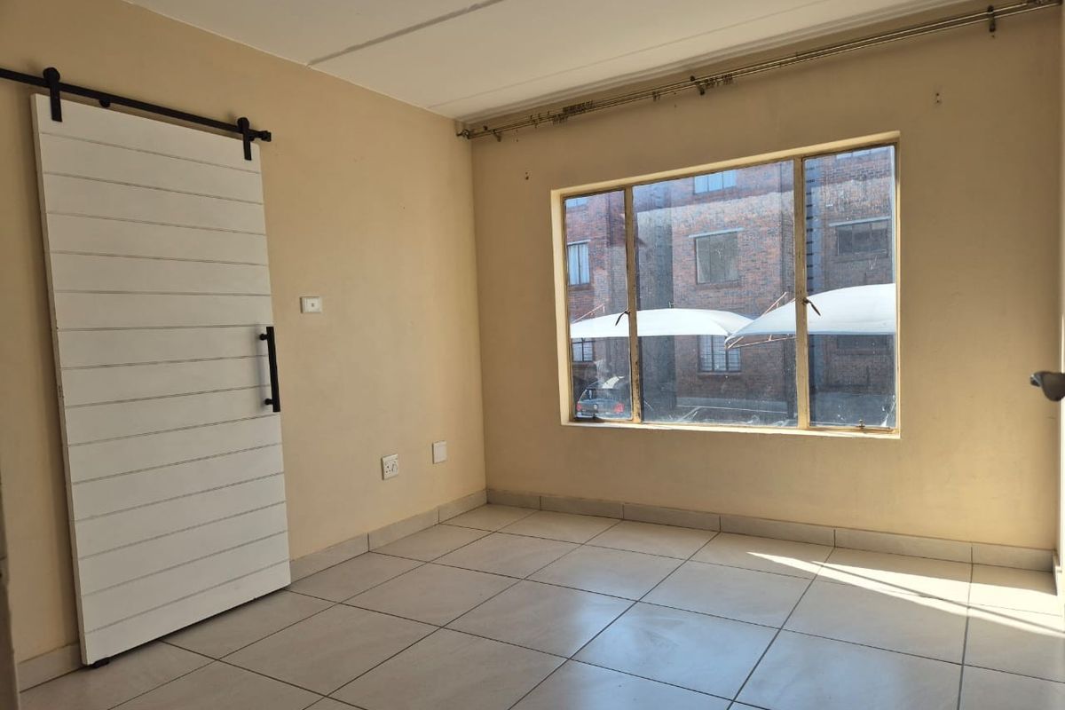 A bright, empty bedroom featuring tiled flooring, a modern white sliding barn door, and a large window providing natural light.
