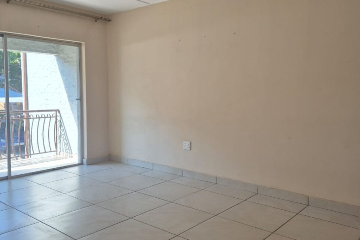 An empty living room featuring neutral ceramic floor tiles, a flush-mount ceiling light, and sliding glass doors leading to a balcony.