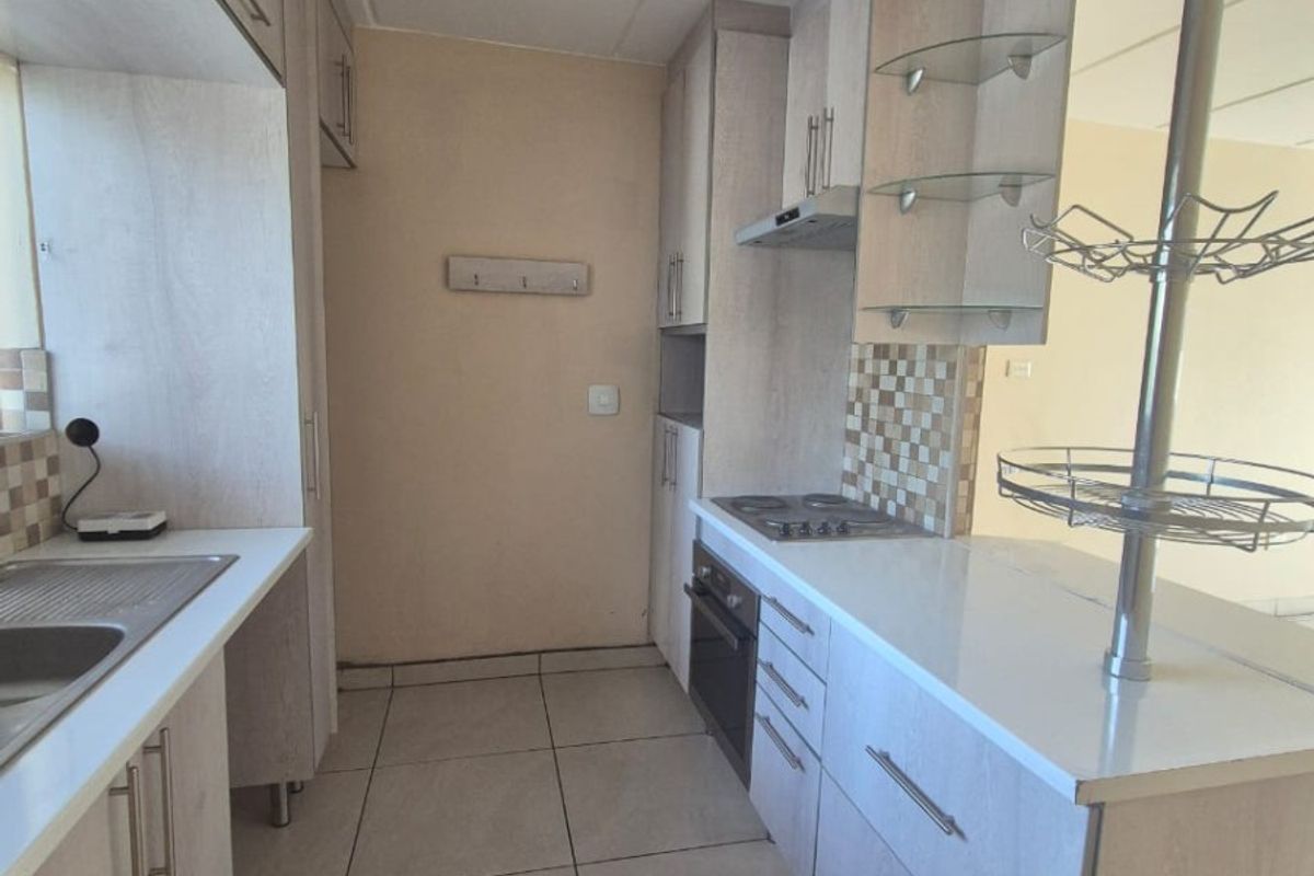 A functional galley-style kitchen featuring light wood-tone cabinetry, tiled flooring, a built-in oven, and a hob with an integrated extractor fan.
