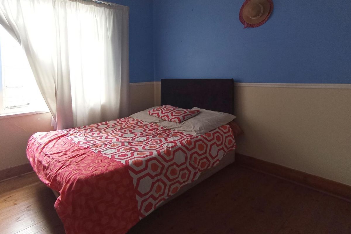 A bedroom featuring timber flooring, two-tone wall paint with a dado rail, and a window with natural light.