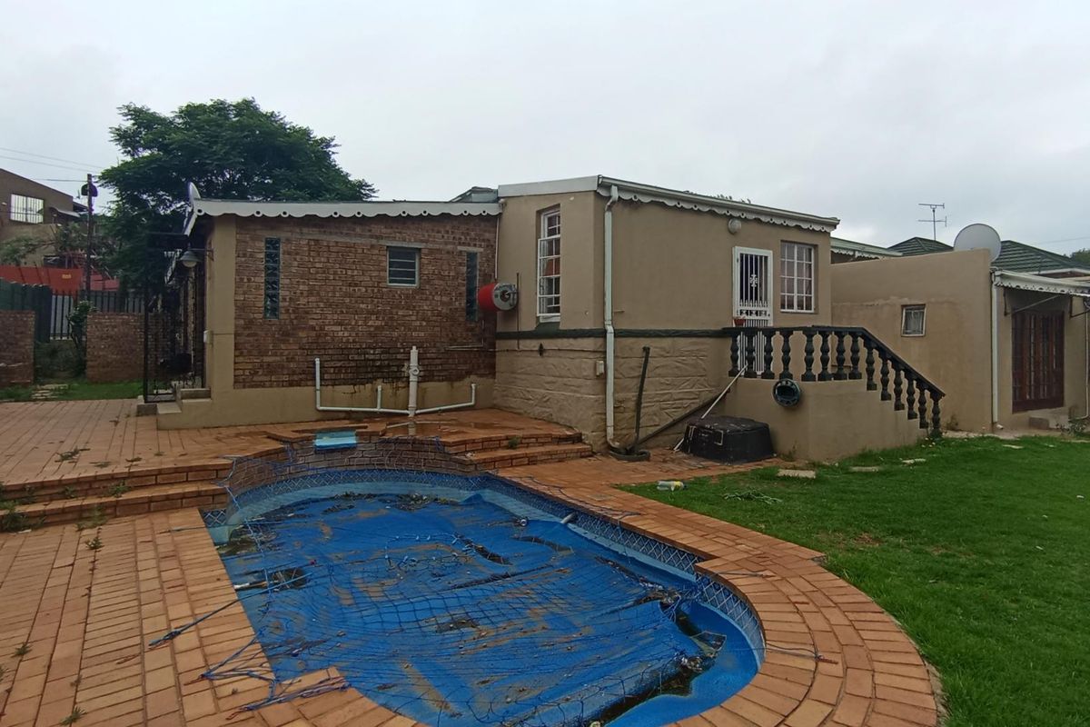 Rear exterior view featuring a swimming pool with a cover, brick and plastered walls, and a raised patio area with balustrades.
