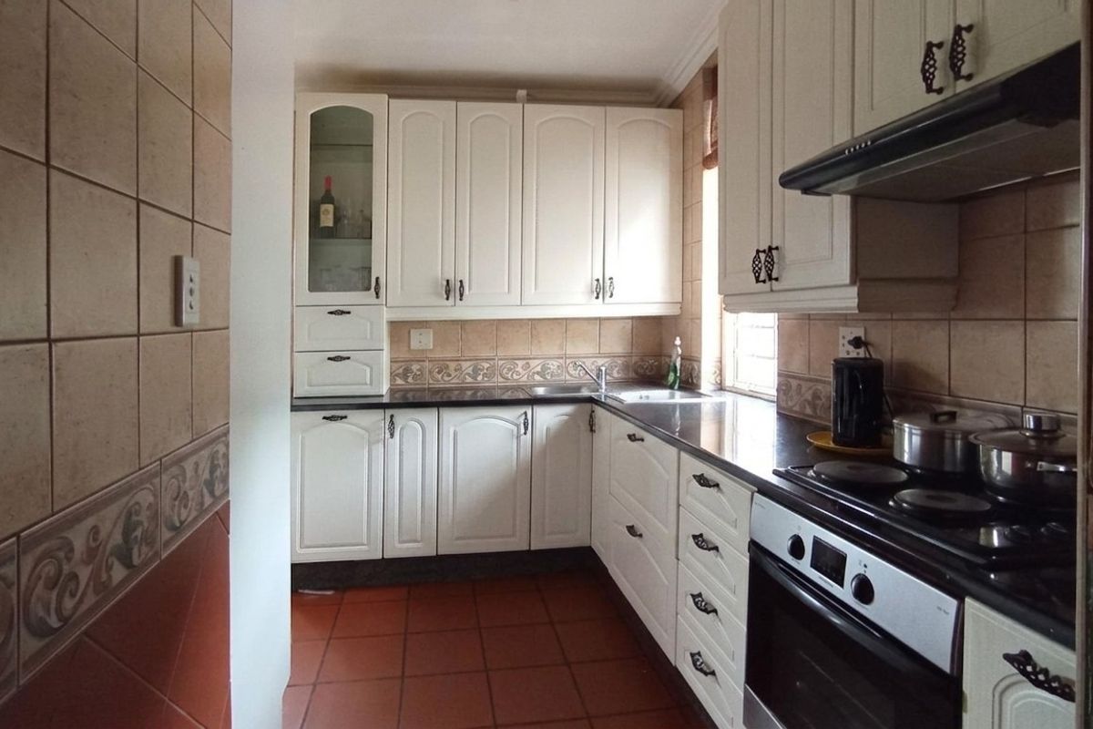 A functional kitchen featuring white cabinetry, dark countertops, a built-in oven with extractor fan, and tiled flooring.