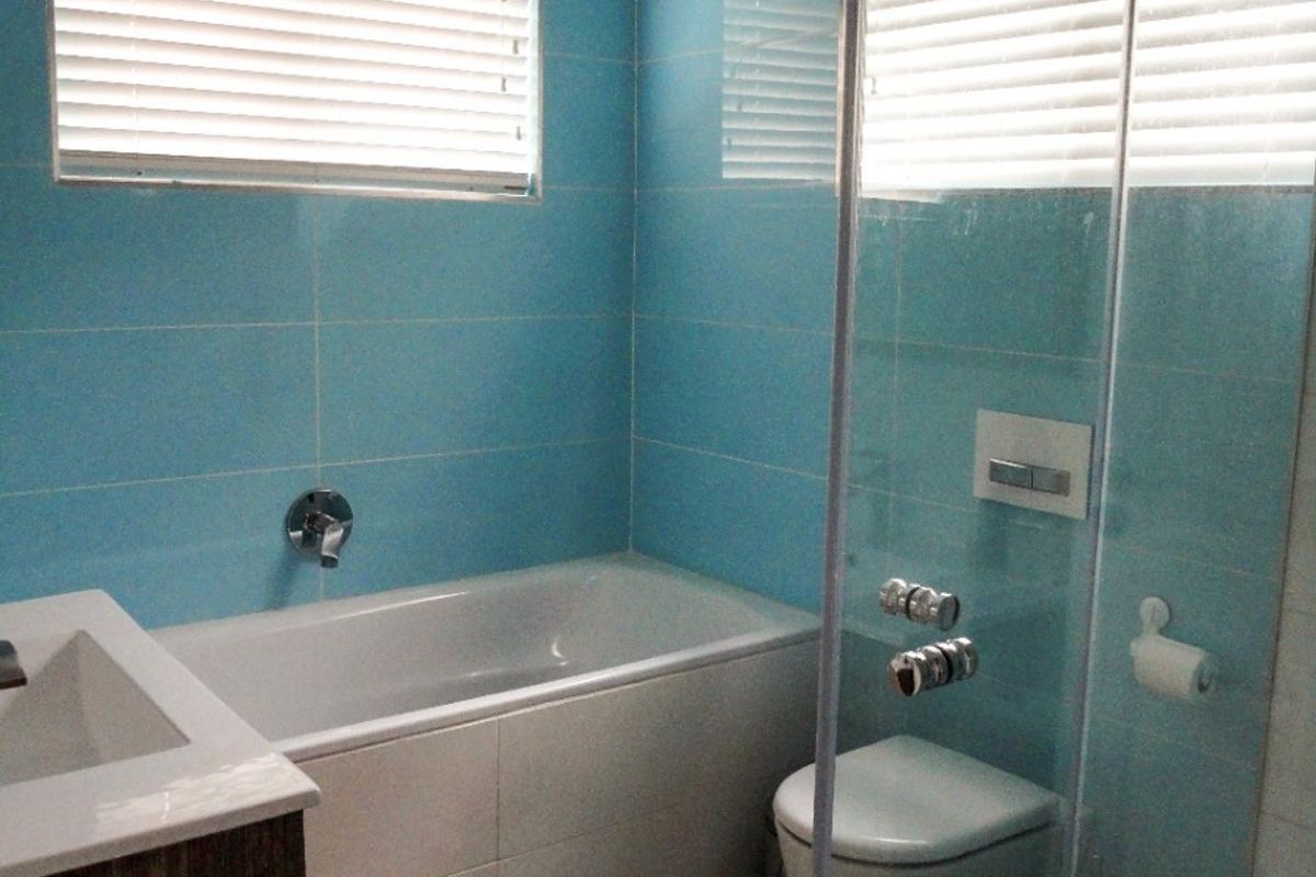 A modern bathroom featuring blue tiled walls, a built-in bathtub, a wall-mounted toilet, and a glass-enclosed shower area with a vanity unit.