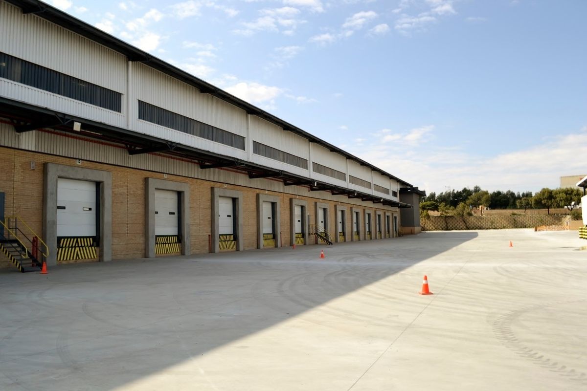 Industrial warehouse exterior featuring multiple loading docks with sectional overhead doors and a spacious concrete yard area.