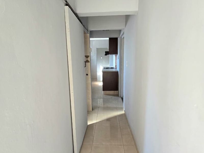 A narrow interior hallway featuring tiled flooring and a sliding door, leading towards a kitchen area with dark cabinetry.