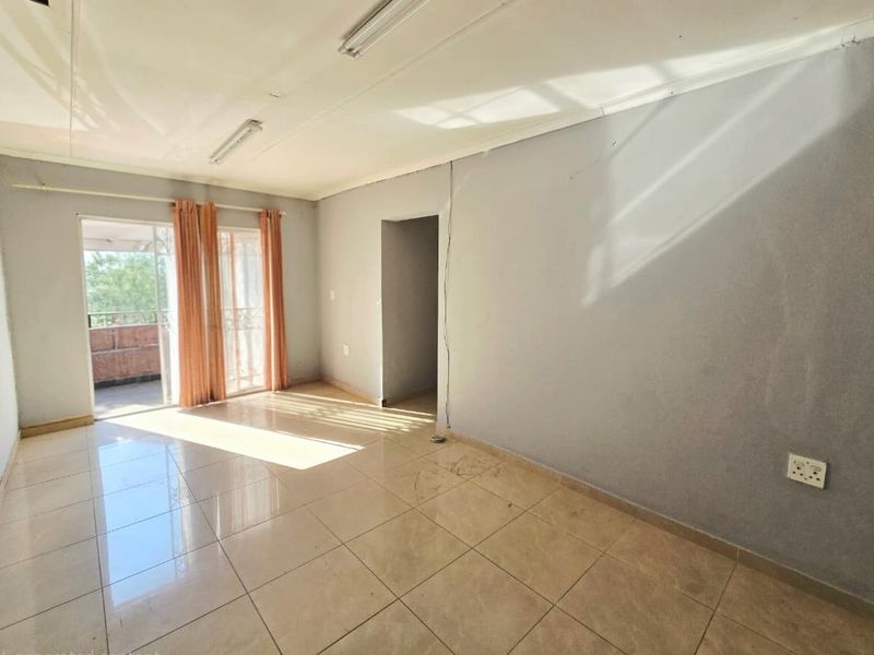 A vacant living room featuring tiled flooring, sliding glass doors leading to a balcony, and neutral wall finishes.