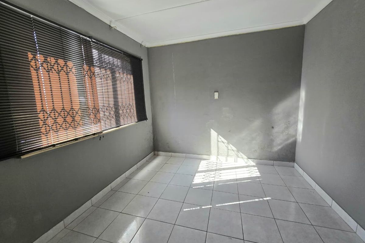An empty bedroom featuring grey painted walls, white tiled flooring, and fitted window blinds with security bars.