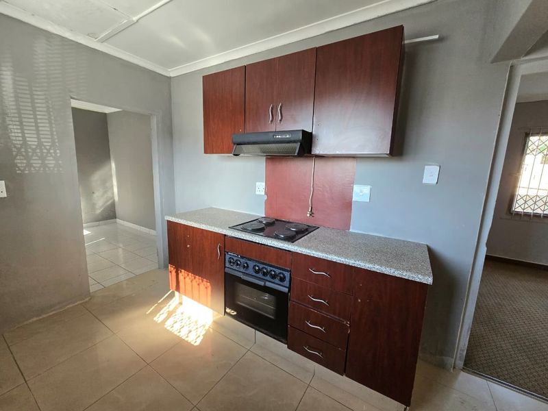 A functional kitchen featuring dark wood cabinetry, a built-in oven, electric hob, and extractor fan, set against a neutral tiled floor.