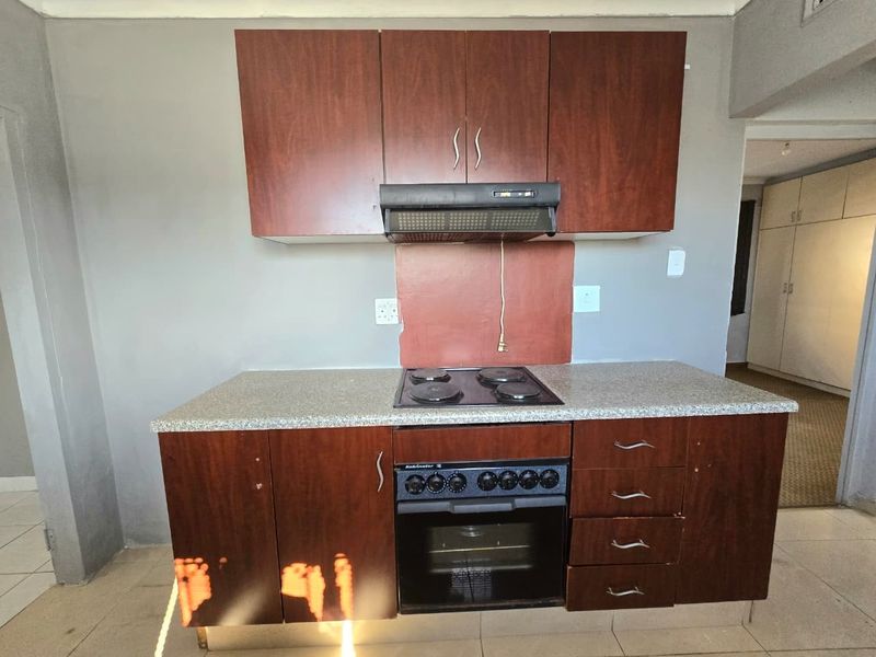 A compact kitchen area featuring dark wood-toned cabinetry, a built-in oven with electric hob, and an overhead extractor fan.