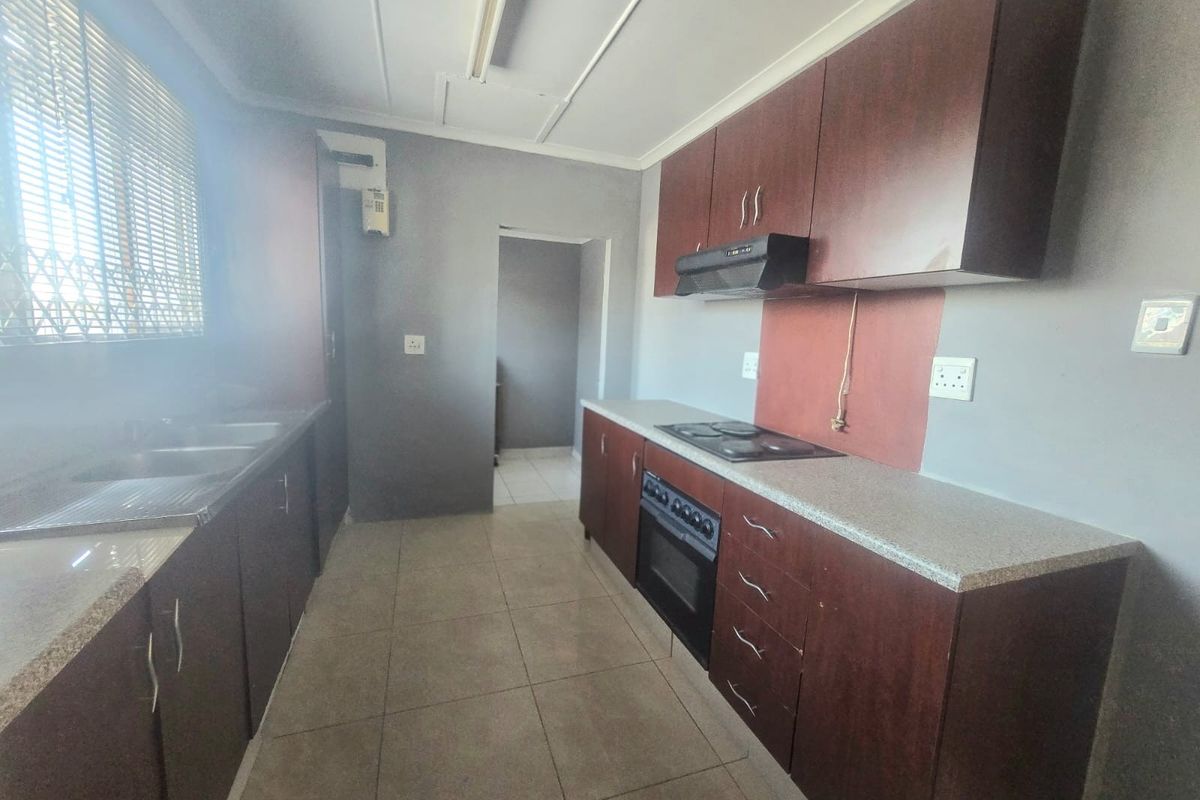 A functional kitchen featuring dark wood cabinetry, stone-look countertops, a built-in oven, and a hob with an extractor fan.