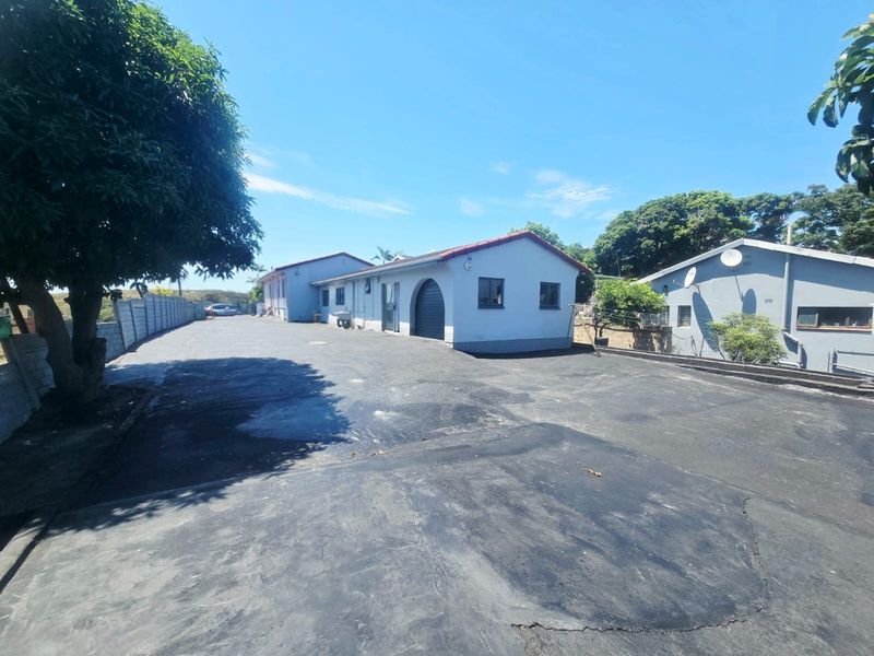 Exterior view of the cottage property featuring a large asphalt driveway, arched entryway, and surrounding boundary walls.