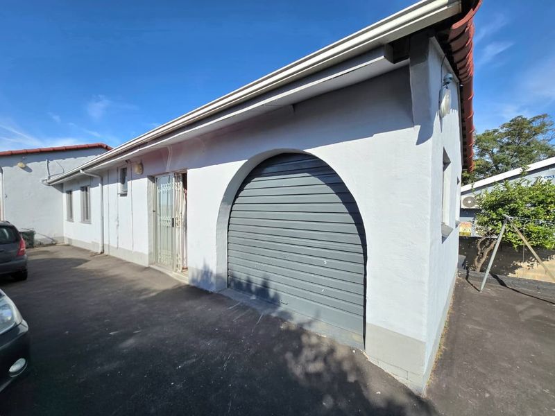 Exterior view of the cottage featuring a grey arched garage door, paved driveway, and white rendered walls under a tiled roof.