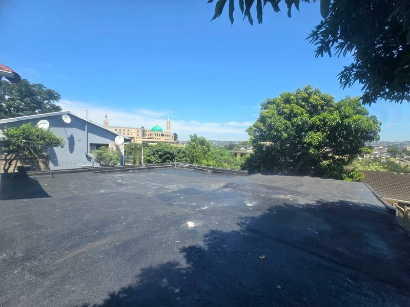 An elevated view of a flat roof surface with a bitumen membrane finish, overlooking the surrounding neighborhood and local landscape.