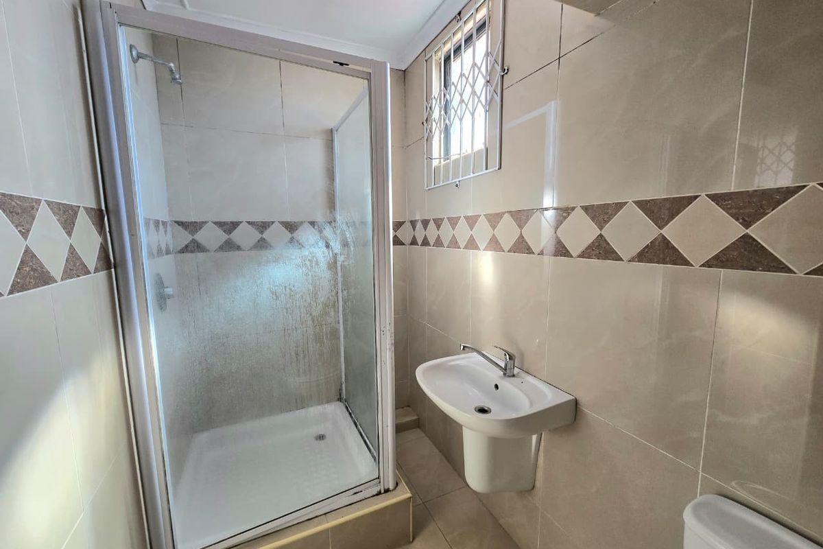 A functional bathroom featuring a tiled shower enclosure, a wall-mounted pedestal basin, and a window with security bars.