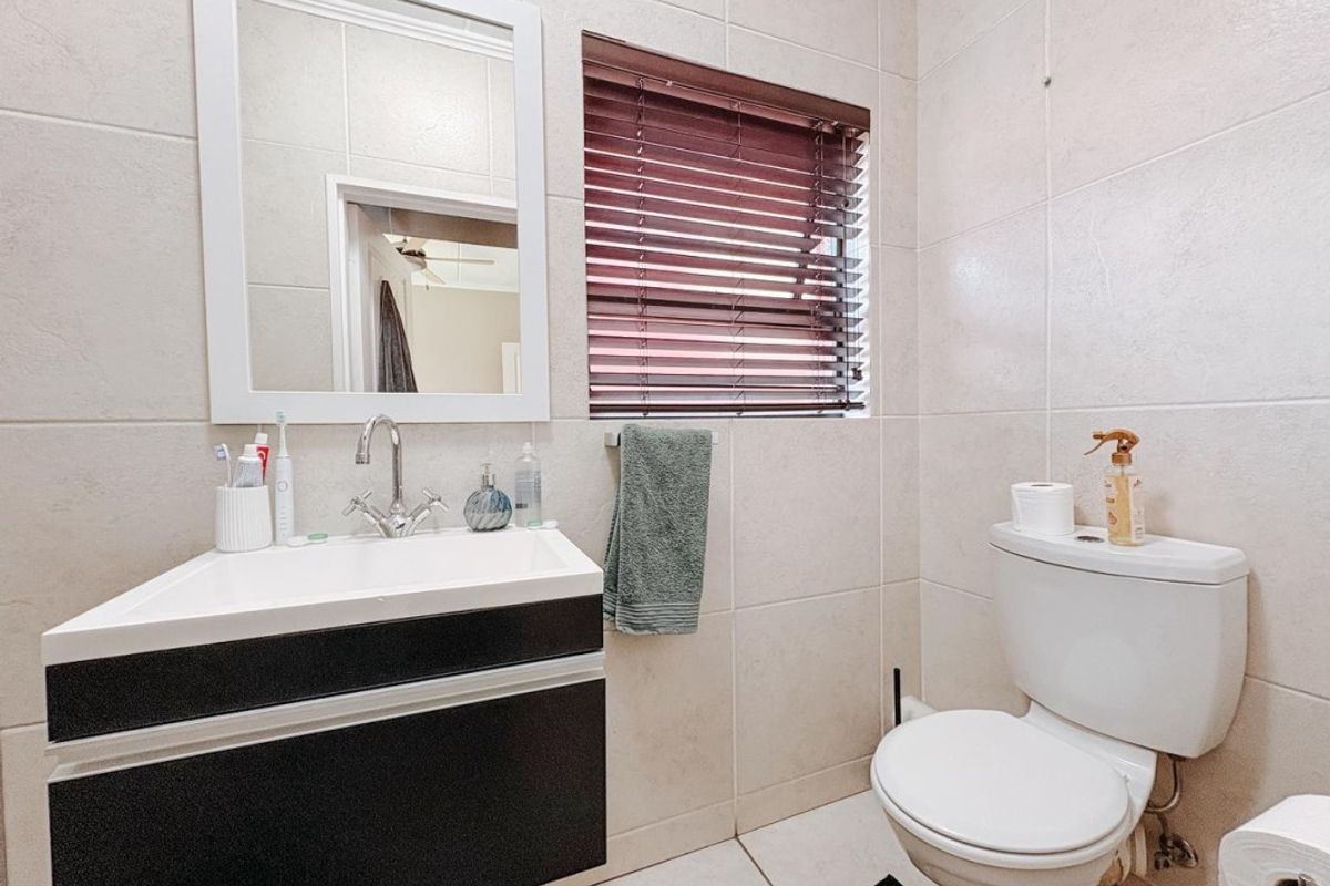 A compact bathroom featuring a modern wall-mounted vanity with a basin, a white toilet, and neutral wall tiling with a window.
