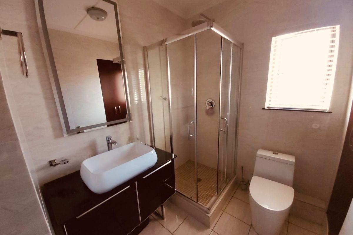 Modern bathroom featuring a glass-enclosed shower, a contemporary vessel sink vanity, and a sleek toilet with neutral wall and floor tiling.