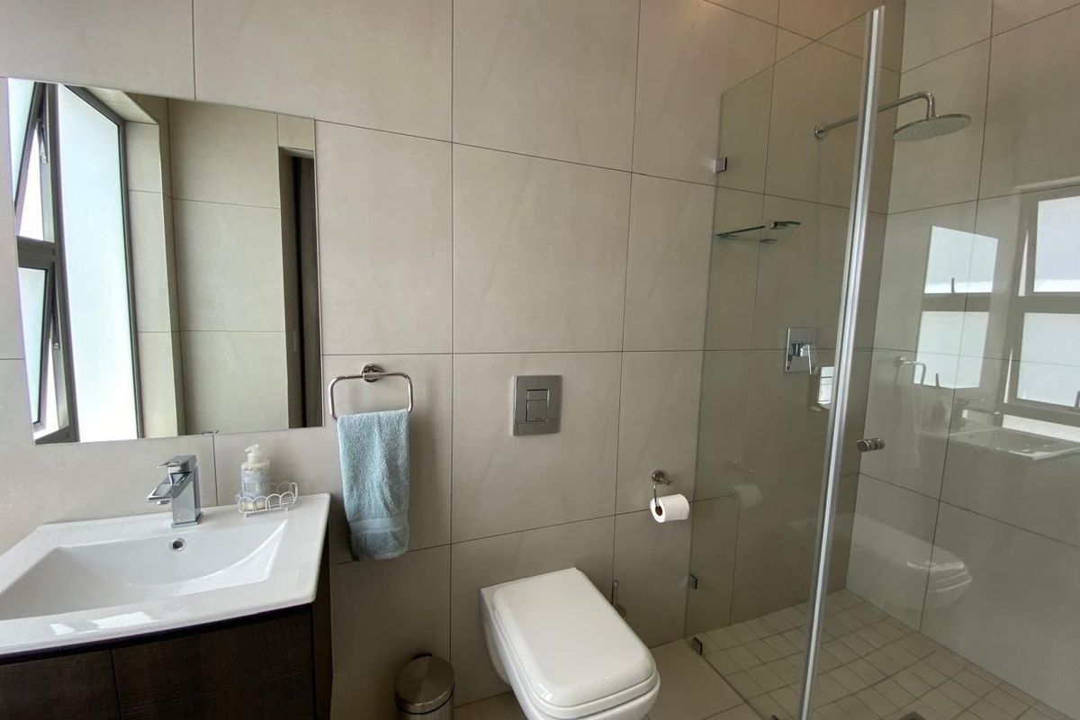 Modern bathroom featuring a wall-mounted toilet, glass-enclosed walk-in shower, and a vanity with a basin and mirror.