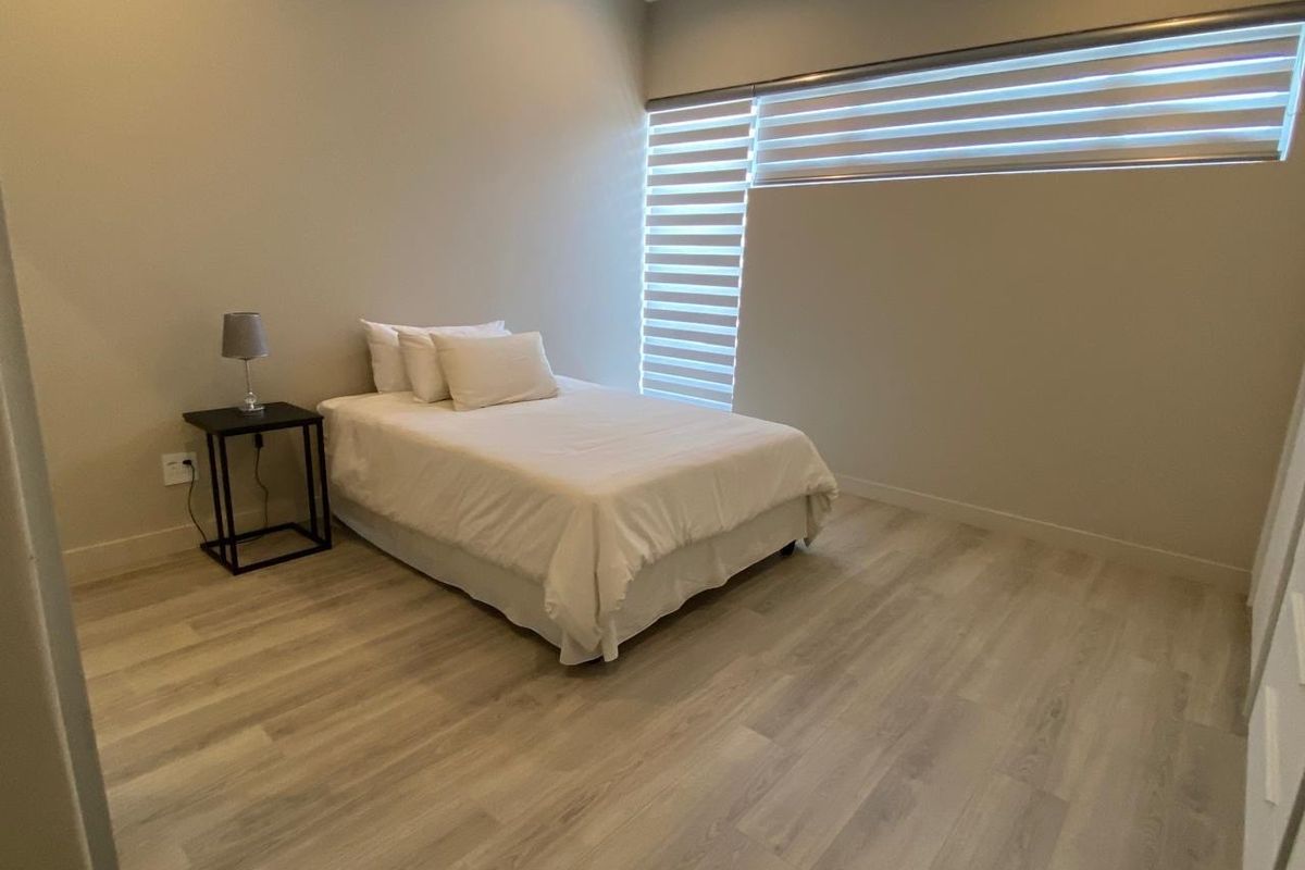 A bright and modern bedroom featuring light-toned wood-look flooring and contemporary horizontal blinds.