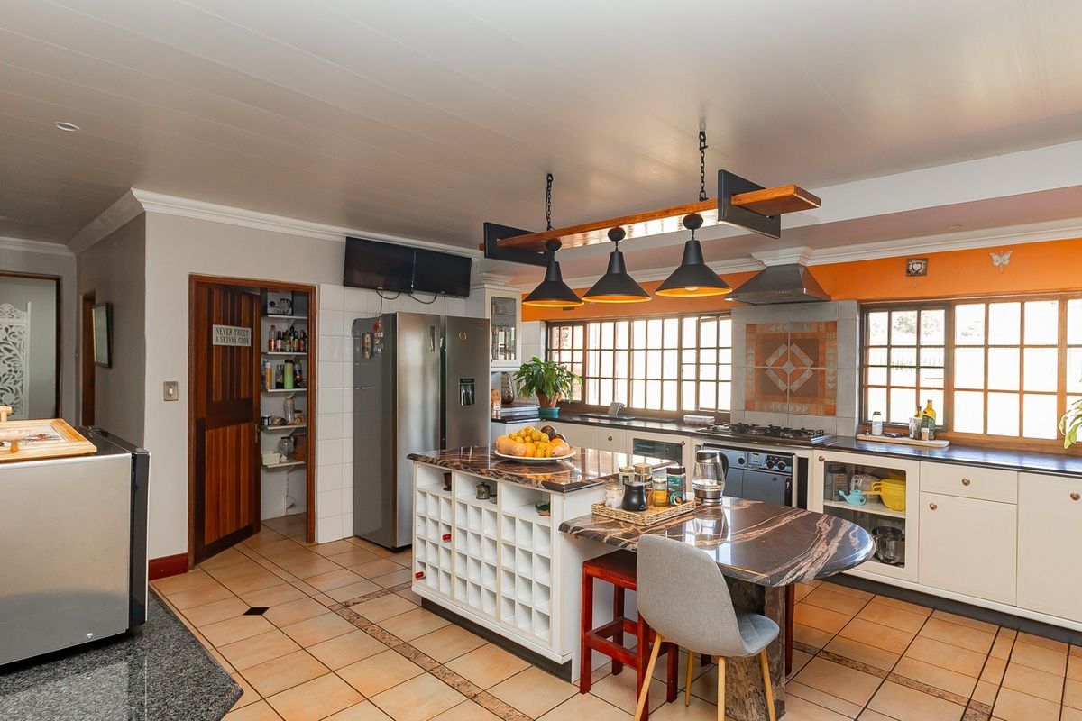 Spacious kitchen featuring a central island with integrated wine storage, stone countertops, built-in oven, extractor fan, and an adjacent walk-in pantry.