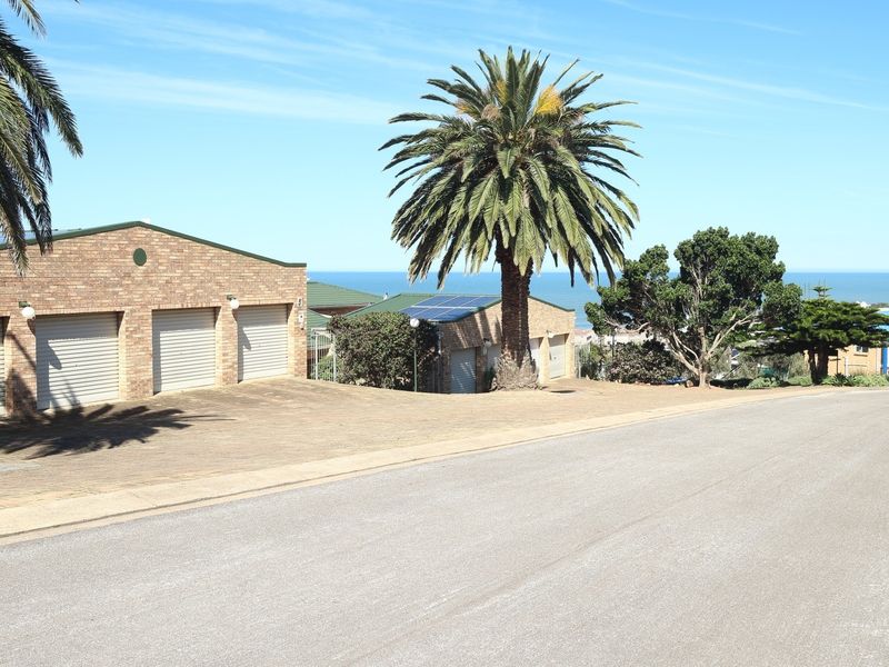Street view of a residential property featuring a triple garage, solar panels, and a paved driveway with ocean views in the background.
