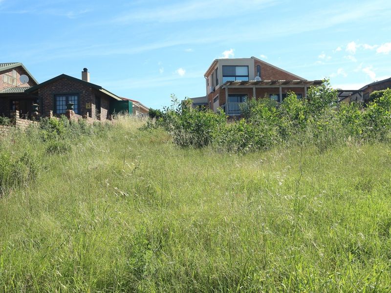 A view of a vacant residential plot with natural grass cover, situated in a developed neighborhood with surrounding houses.
