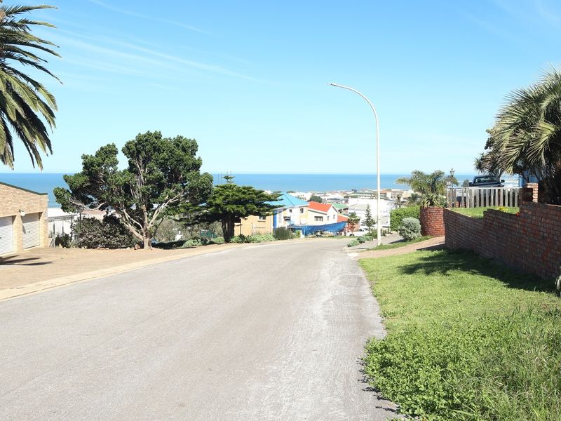 A street view of the residential area showing the road, surrounding landscaping, and distant ocean views.